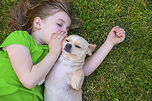 young girl laying in grass telling a secret to a dog